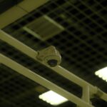 Close-up of a ceiling-mounted security camera in an indoor environment with grid and lights.